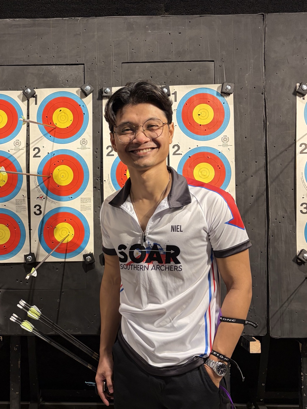 Niel Lat smiling at the archery range, tournament target faces behind him